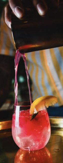 A vivid pink cocktail being poured into a garnished glass