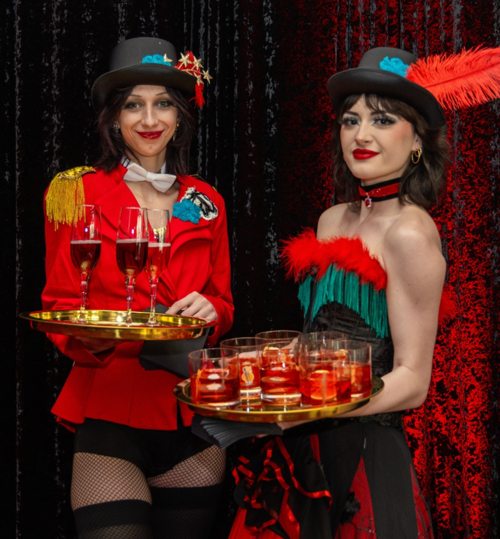 Two team members in theatrical costumes presenting trays of drinks